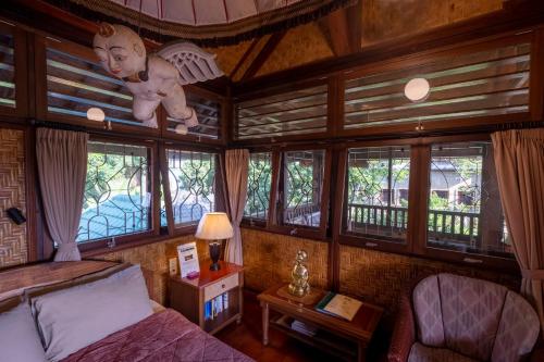 a bedroom with a bed and a chair and windows at Murni's Houses & Spa in Ubud