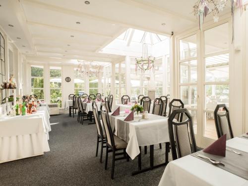 a restaurant with white tables and chairs and windows at Hennedamm Hotel in Meschede
