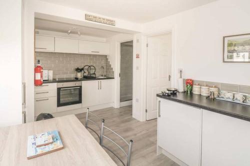 a kitchen with white cabinets and a table in it at Hegarty's cottage at Trevarrian Lodge in Mawgan Porth