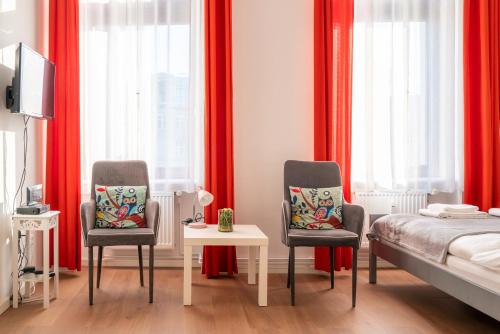 twee stoelen en een tafel in een slaapkamer met rode gordijnen bij City Studio Apartment for 2, near Sonnenallee in Berlijn