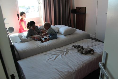 a woman and two children sitting on a bed at Hôtel The Originals City Le Berry - proche centre-ville - Gare in Bourges