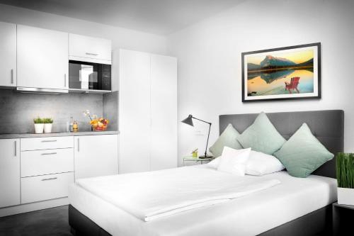 a white bedroom with a large bed and a kitchen at Favorit Serviced Apartments in Ludwigsburg