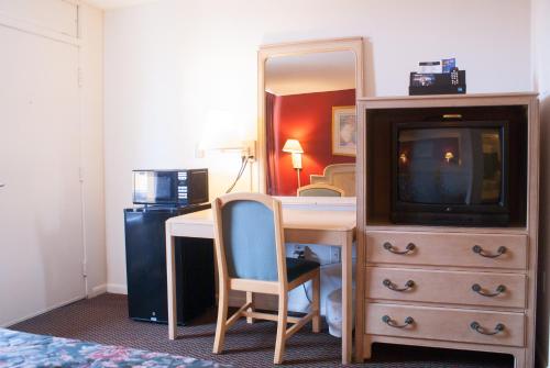 a room with a desk with a tv and a dresser at Scottish Inn Downtown Jacksonville in Jacksonville