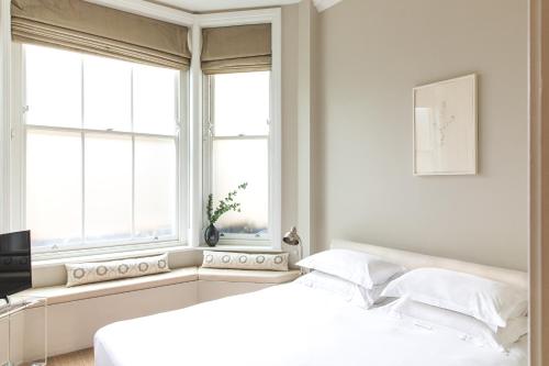 a white bedroom with two beds and two windows at 56 Welbeck Street in London