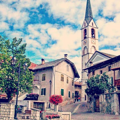 a church with a tower with a clock on it at Da Rinota in Alta Val di Non in Malosco