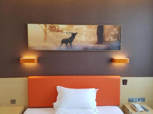 a painting of a deer on a wall above a bed at 7Days Premium Yantai Penglai New Bus Station Branch in Penglai