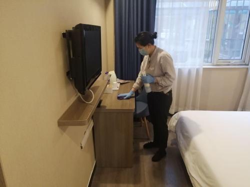 a woman standing in a hotel room with a phone at 7Days Premium Beijing Zhongguancun Renmin University Suzhou Street Subway Station Branch in Beijing