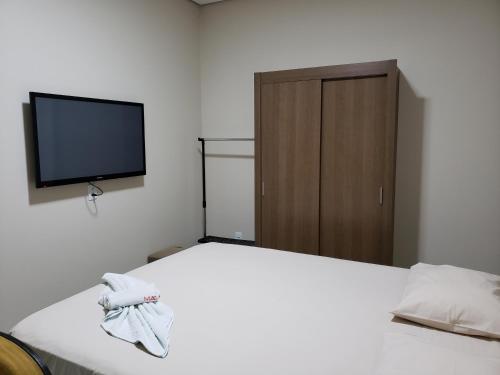 a bedroom with a white bed with a tv on the wall at Flat Genoveva in Tangara da Serra