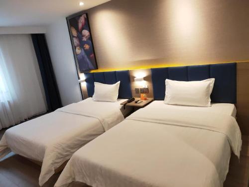 2 camas en una habitación de hotel con sábanas blancas en 7Days Premium Yibin North Gate Bus Station Branch, en Yibin