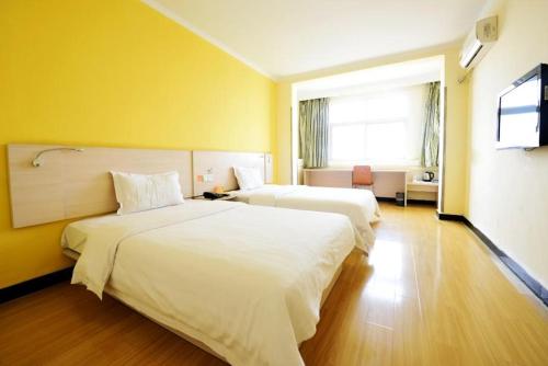 two beds in a hotel room with yellow walls at 7Days Inn Kaifeng Gulou Square Xueyuanmen in Kaifeng