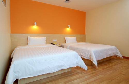 two beds in a room with an orange wall at 7Days Inn Chenzhou West High Speed Railway Station in Chenzhou