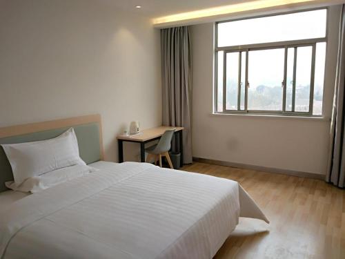 a bedroom with a bed and a desk and a window at 7Days Inn Chizhou Jiuhuashan Branch in Chizhou