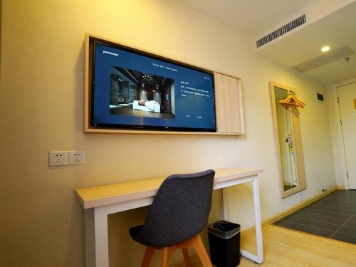 a television hanging on a wall with a chair at 7Days Inn Zhaotong Academy Fada Square Branch in Zhaotong