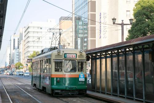 a green tram on a city street with buildings at Hotel S-Plus Hiroshima Peace Park in Hiroshima