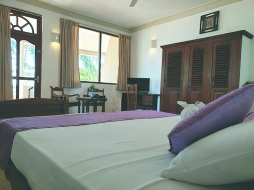 a bedroom with a large white bed with purple pillows at Oasey Ayurveda Hotel in Bentota