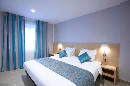 a bedroom with a large white bed with blue pillows at The Originals City, L'Haut' Aile, Coquelles-Calais Tunnel s/Manche L'HAUTAILE in Coquelles