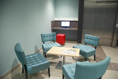a waiting room with chairs and a table and a tv at The Originals City, L'Haut' Aile, Coquelles-Calais Tunnel s/Manche L'HAUTAILE in Coquelles