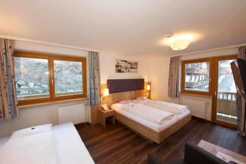 a bedroom with two beds and two windows at Johanneshof - Dein MOUNTAIN Wohlfühlhotel in Saalbach Hinterglemm