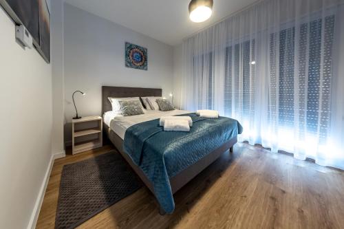 a bedroom with a bed with a blue blanket and windows at Apartament Margo in Łeba