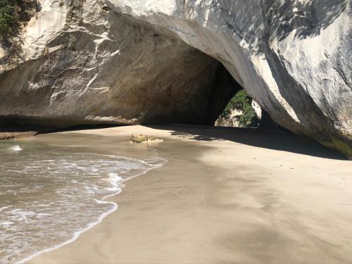 a sandy beach with a large rock formation at Hahei Beach Bach. in Hahei