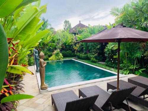a swimming pool with an umbrella and chairs and a fountain at Villa D'Uma in Ubud