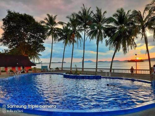 einen Pool mit Palmen und dem Meer im Hintergrund in der Unterkunft Jansom Beach Resort in Ranong