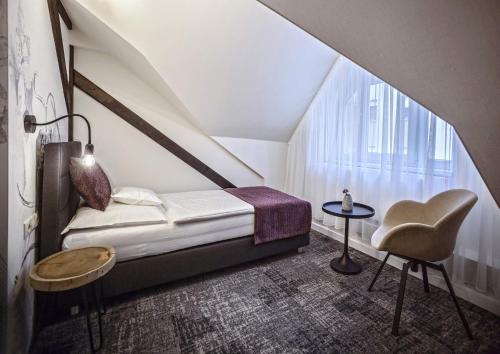 a bedroom with a bed and a chair and a window at Piccolo Panzió Vendéglő Vinoteca in Zalaegerszeg