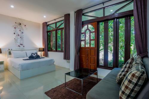 ein Schlafzimmer mit einem Bett, einem Sofa und Fenstern in der Unterkunft Brodie Rawai Resort in Rawai Beach