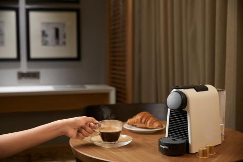 a person holding a cup of coffee next to a coffee maker at The Residency Towers Puducherry in Puducherry