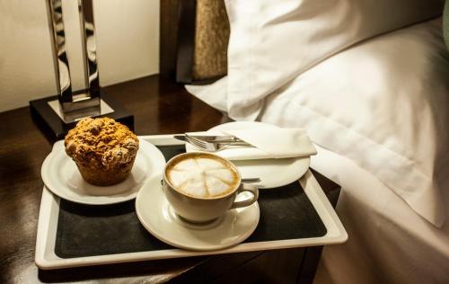 a tray with a cup of coffee and a muffin on a bed at Avani Lesotho Hotel & Casino in Maseru