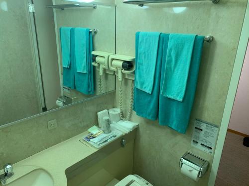 ein Badezimmer mit blauen Handtüchern, einem Waschbecken und einem Spiegel in der Unterkunft Suzuka Storia Hotel in Suzuka