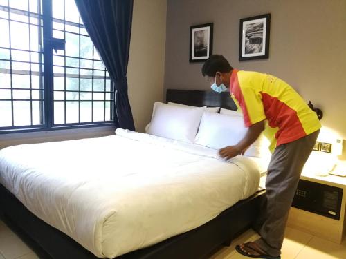 a man is making a bed in a hotel room at JV Hotel @ Simpang Ampat in Simpang Ampat