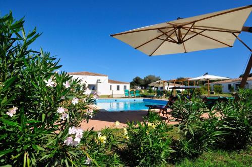 a pool with a tan umbrella and a chair and a table at Hotel Baia Cea in Bari Sardo