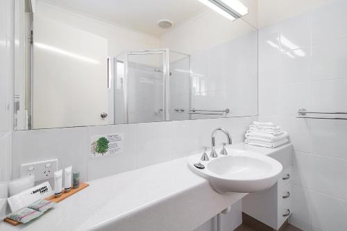 Heritage Motor Inn Corowa في كوروا: حمام أبيض مع حوض ومرآة