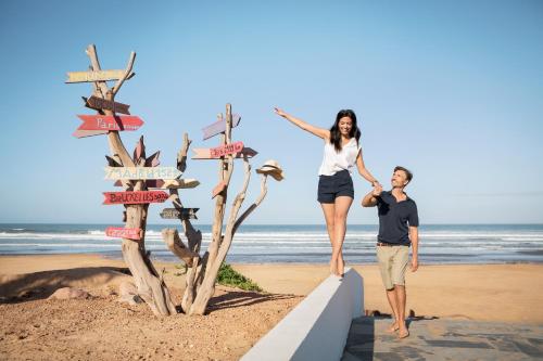 a man and woman standing next to a directional sign on the beach at ROBINSON AGADIR - All Inclusive in Agadir