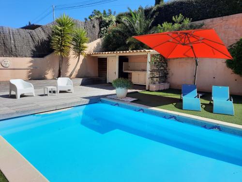 een zwembad met een rode parasol en twee stoelen en een huis bij Villa Madysan à St Aygulf, plage et mer à 900m, piscine chauffée, jardin privé in Saint-Aygulf