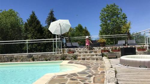 una mujer parada junto a una piscina con sombrilla en Bungalow de 3 chambres avec piscine partagee terrasse amenagee et wifi a Argences en Aubrac, en Banes