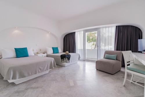 a white bedroom with two beds and a chair at Las Hadas by Brisas in Manzanillo