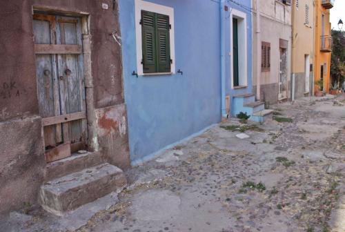 an alley with a blue building and a door at Bosa Guest House in Bosa