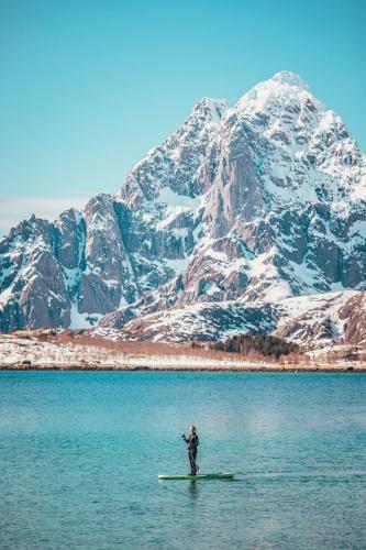 a man on a paddle board in the water with a mountain at Skårungen - Hotel, Cabins and Camping in Kabelvåg