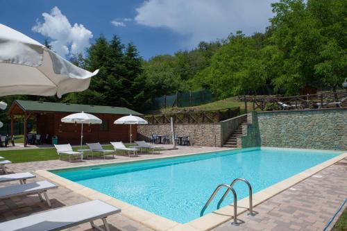 a swimming pool with chairs and umbrellas next to it at Il Borgo Dei Corsi - Charming Holiday Apartments in Ortignano Raggiolo