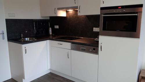 a kitchen with white cabinets and a microwave at De Sprink - Vakantiewoning in Zoutelande