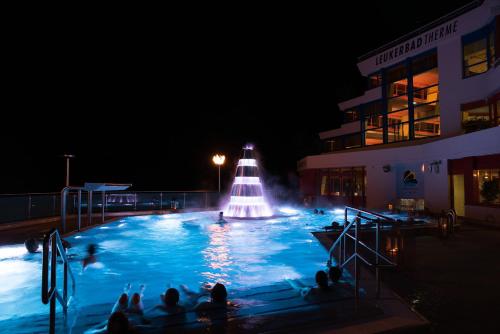 a swimming pool with a fountain at night at Hotel Walliserhof-Leukerbad-Therme in Leukerbad