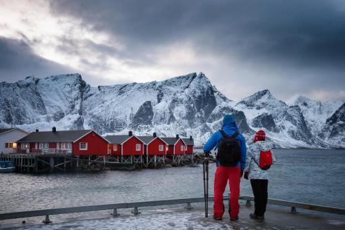 two people standing on a dock with snow covered mountains at Eliassen Rorbuer in Reine