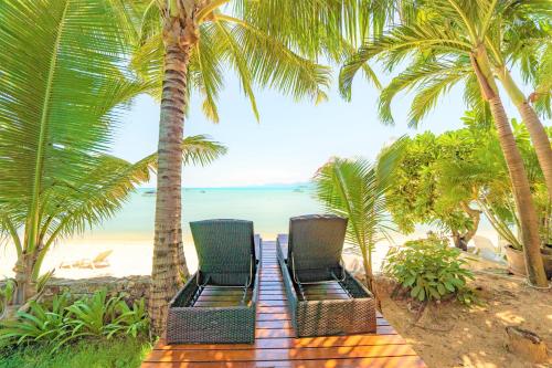 two chairs sitting on a beach with palm trees at Erawan Villa Hotel in Bangrak Beach