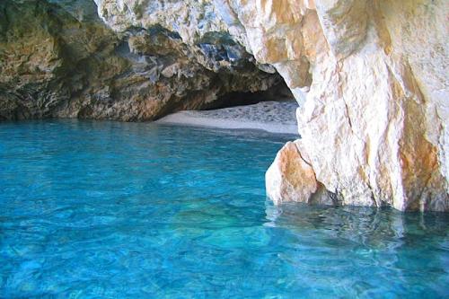 a pool of blue water next to a rock cave at Athenea Villas, Private Pools & Gardens in Keri