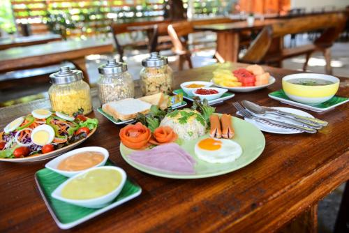 een houten tafel met borden ontbijtproducten erop bij Theerama Cottage in Suan Phung
