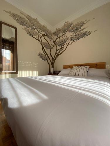 a white bed in a bedroom with a tree on the wall at Vut Carmen in Burgos