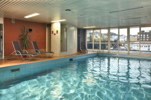 a large swimming pool with two chairs in a building at Concorde Hotel Siegen in Siegen