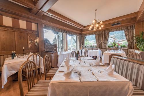 a restaurant with white tables and chairs and windows at Belvedere Dolomites Flower Hotel in Moena